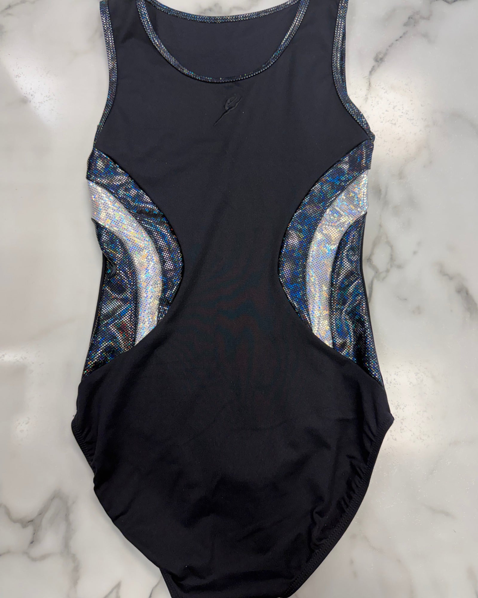 A sleeveless black leotard with metallic blue and silver patterned side panels, laid flat on a white marble surface.