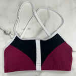 A colorblock dance bra top with a color-blocked design in burgundy, black, and white, featuring thin white crossover shoulder straps, laid flat on a white marble surface.
