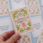 A hand holds a small illustrated card deck box labeled "dancer roulette" with floral borders and pink ballet slippers, against a light blue background with matching cards scattered around.