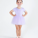 A young girl modeling a light purple ballet leotard with a matching tutu skirt and a matching headband, standing in ballet slippers against a white studio background.