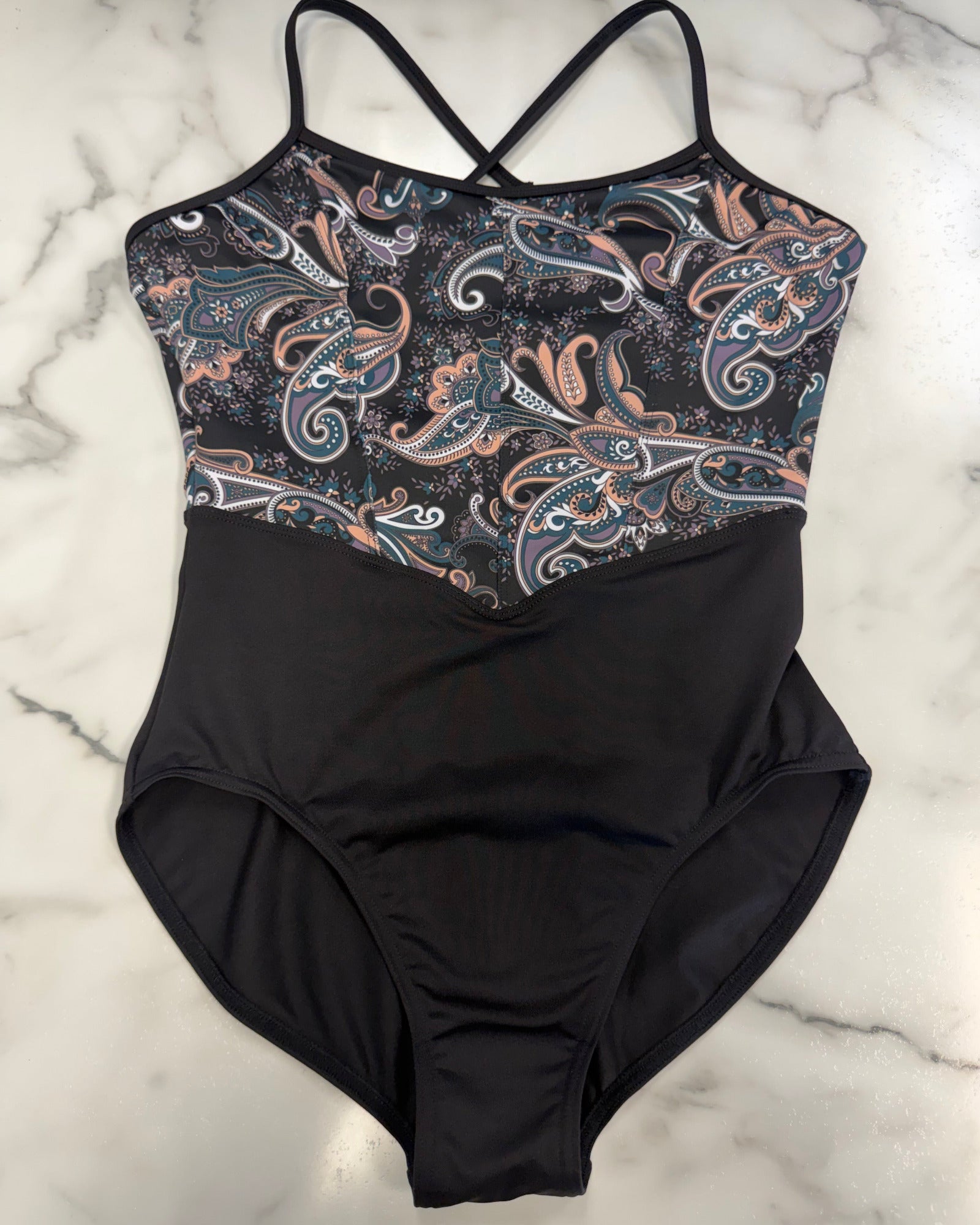 A leotard with a solid black lower body and a black, blue, and peach paisley patterned upper chest, laid flat on a white marble surface.
