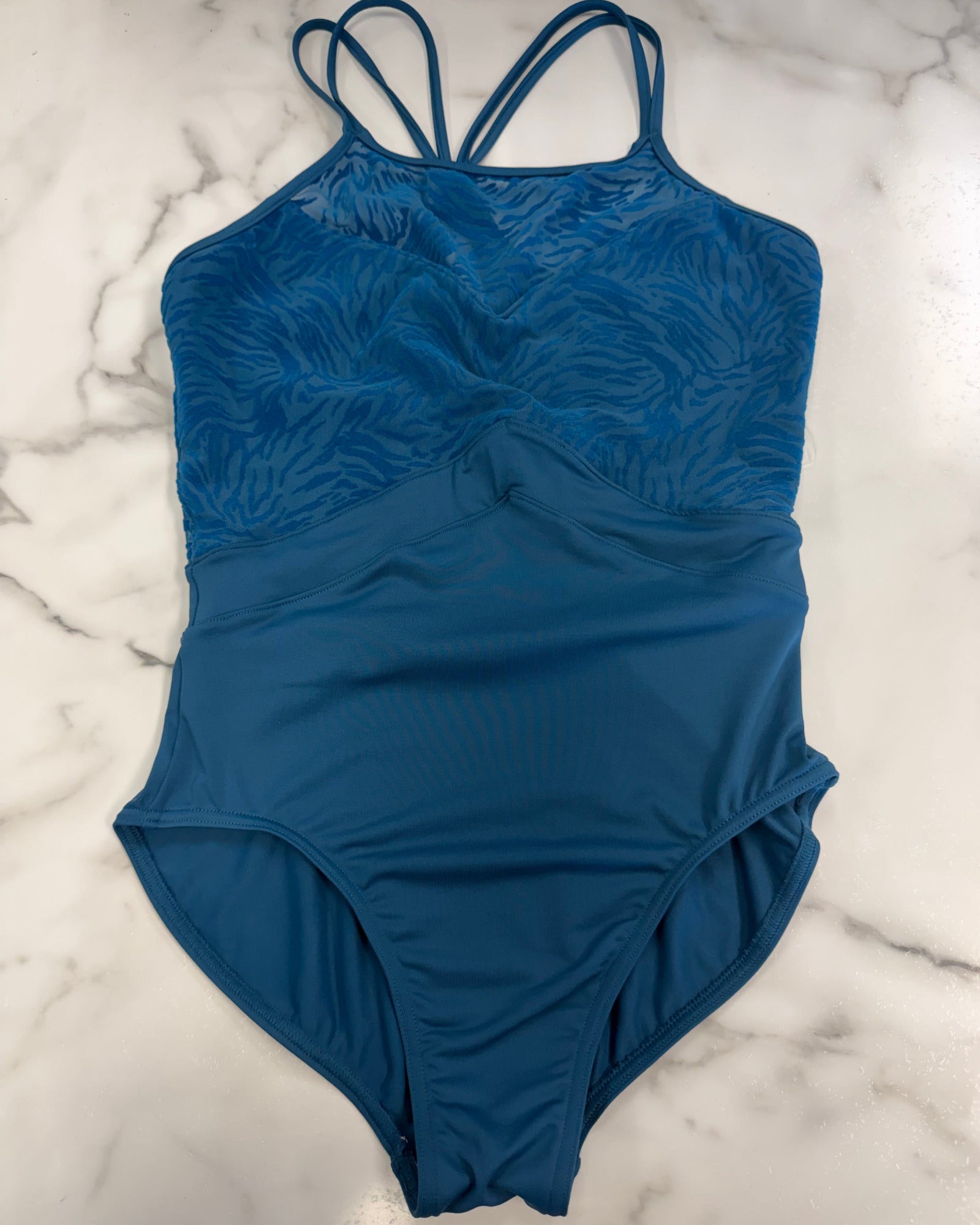 A blue leotard with a textured, tonal zebra pattern on the upper bodice and solid blue straps, laid flat on a white and gray marble surface.