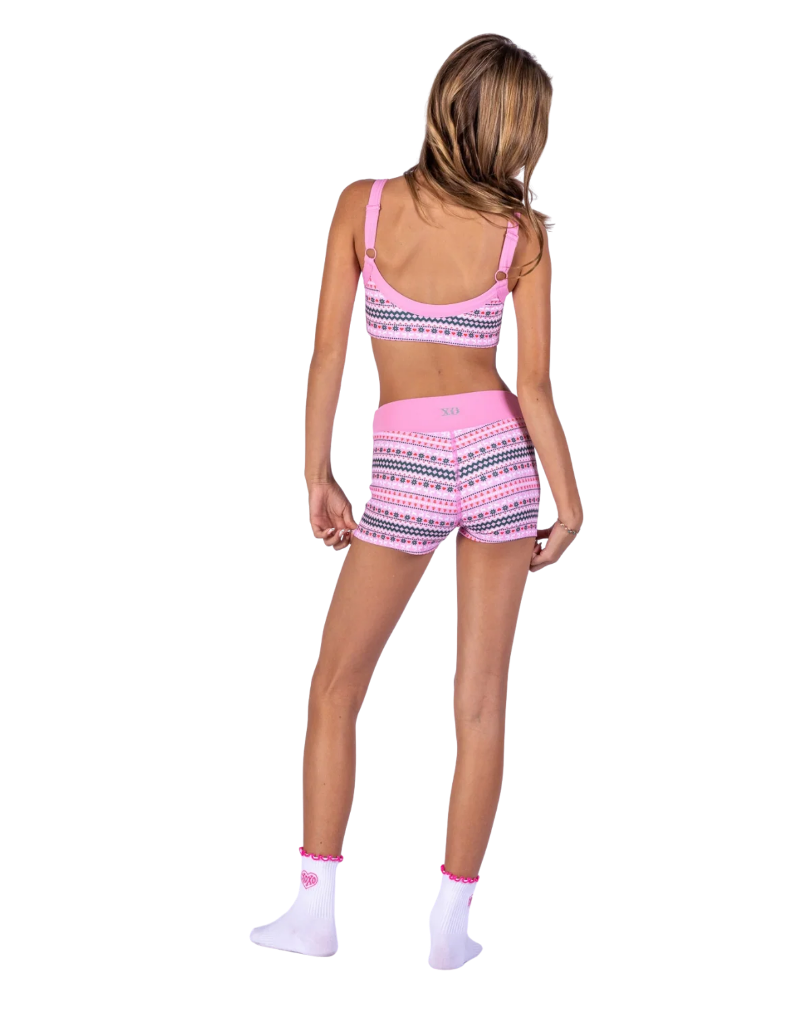 A woman shown from the back wearing a pink two-piece dance outfit with a geometric pattern, featuring a sports bra and matching shorts. The brand name 'XO' is printed on the back waistband of the shorts.