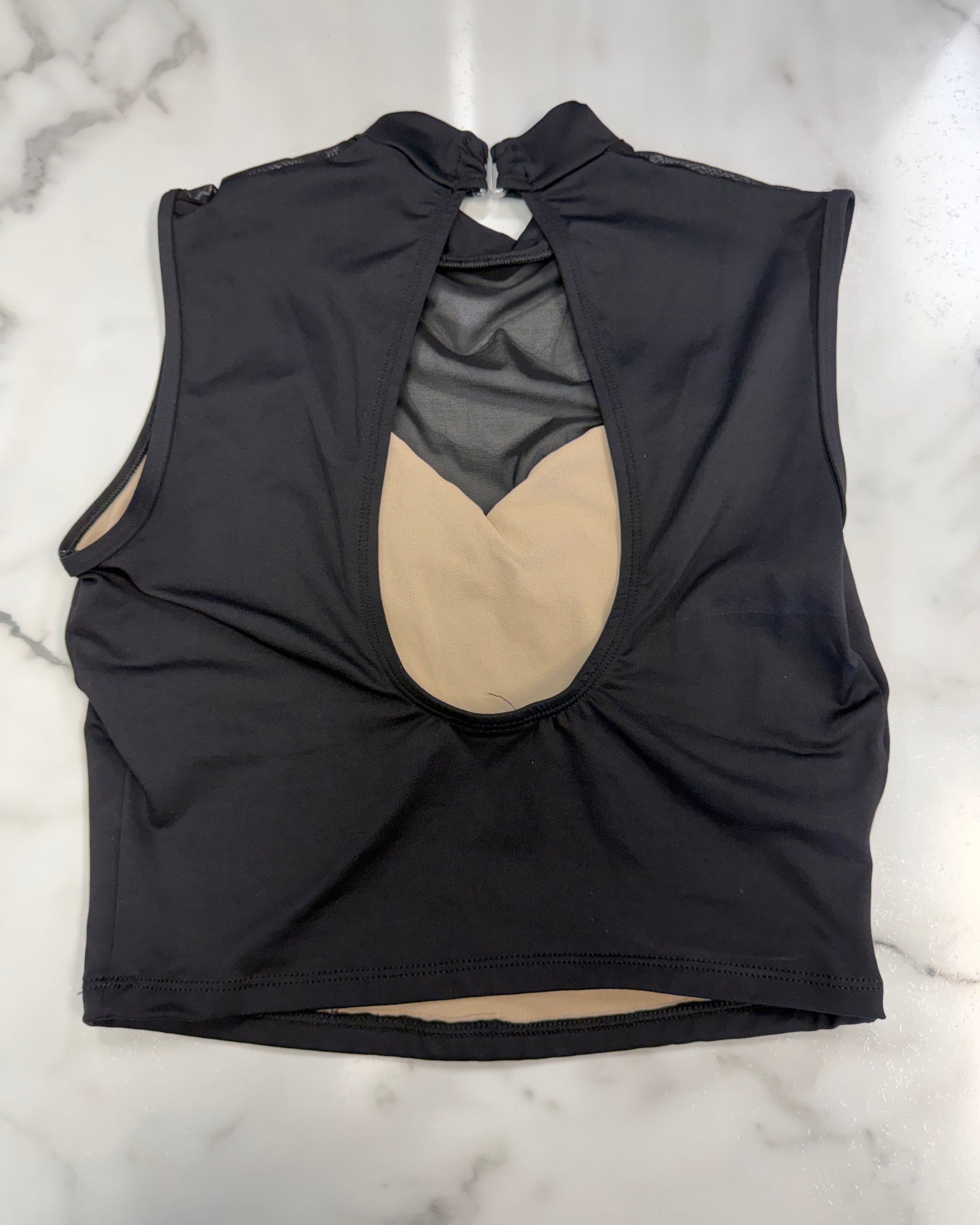 A black sleeveless dance top with a high mock neck and a keyhole open back, shown flat on a white marble surface. Inside is lined in beige.