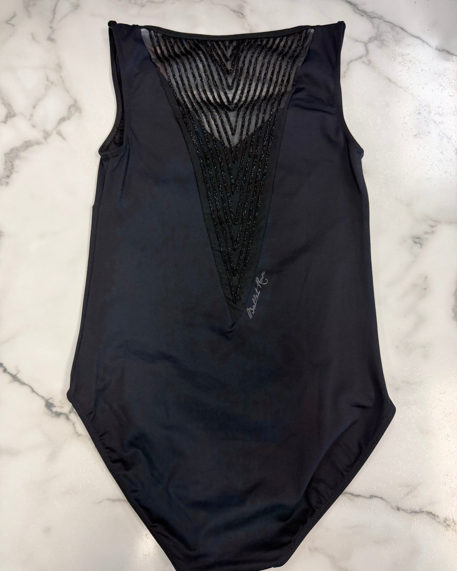 A black sleeveless leotard with a sheer mesh V-neckline and textured black mesh panel, laid flat on a white marble background.
