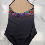 A halter-neck one-piece leotard laid flat on a white marble surface. The leotard features a dark navy-to-black gradient lower body, a colorful abstract floral pattern across the bust and upper waist, and a beige mesh or skin-tone inner lining visible at the neckline.
