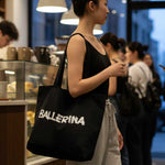 Woman holding a black tote bag with 'BALLERINA' text in a casual setting.