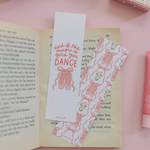 Two decorative paper bookmarks styled on an open book on a pink surface. One bookmark is light pink with pink script text reading 'and the music to make you DANCE' and a pink bow illustration.