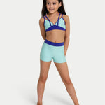 Young girl wearing a blue and green bra top and shorts set on a white background
