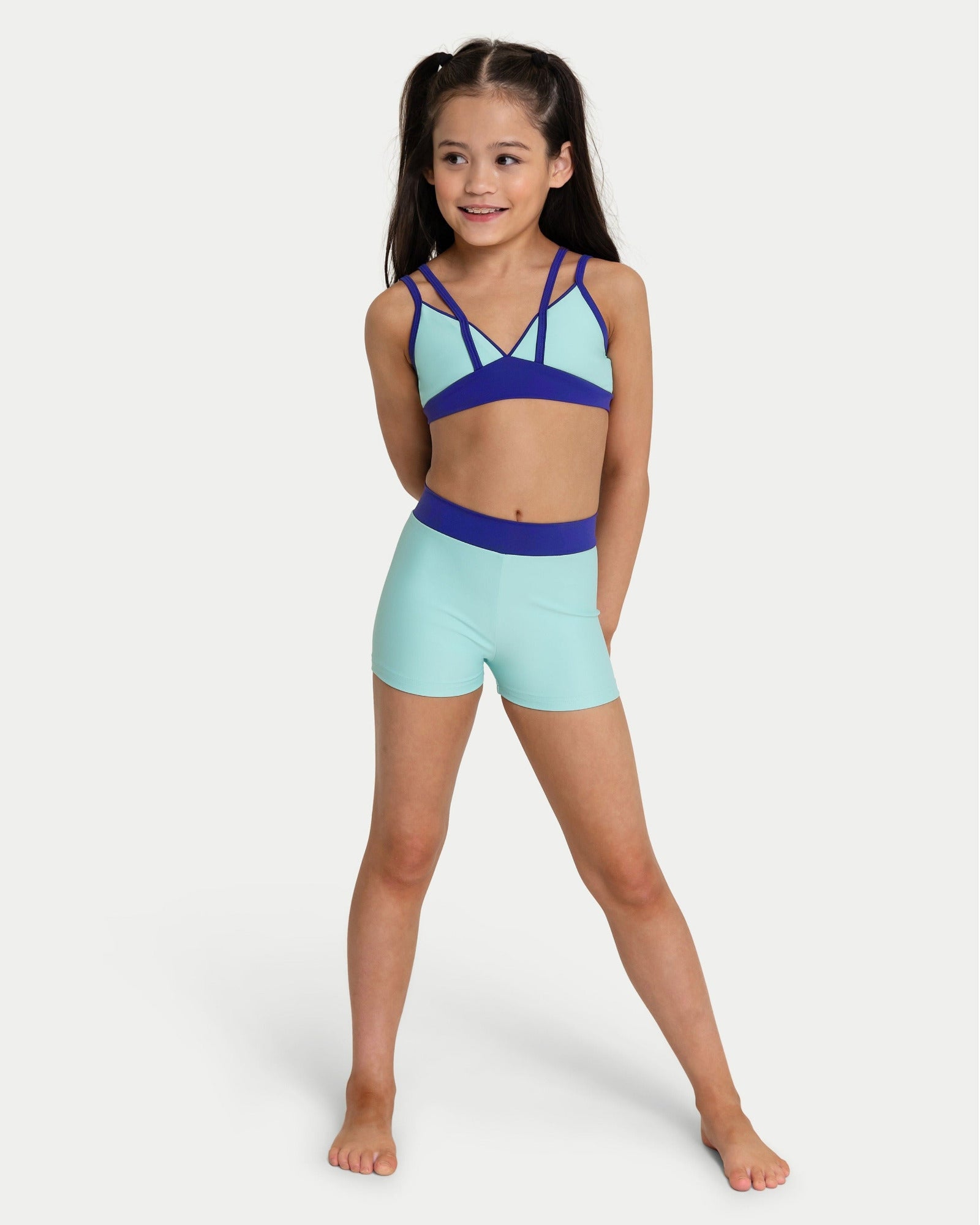 Young girl wearing a blue and green bra top and shorts set on a white background