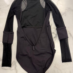 A black long-sleeve dance leotard with mesh sleeves and a deep open back, laid flat on a white marble surface.
