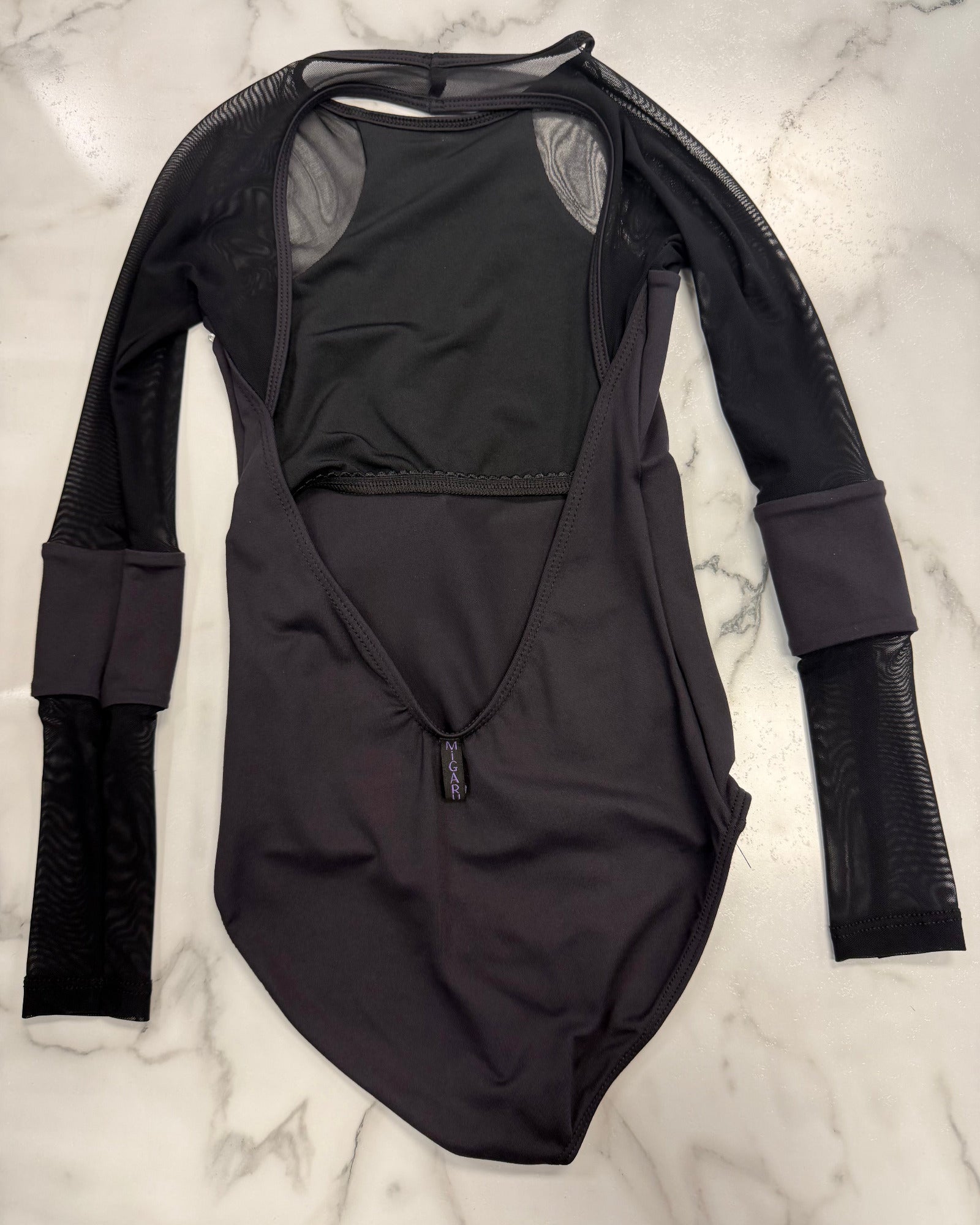 A black long-sleeve dance leotard with mesh sleeves and a deep open back, laid flat on a white marble surface.