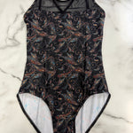 A leotard with a black background and a detailed multicolor paisley pattern, laid flat on a white marble surface.