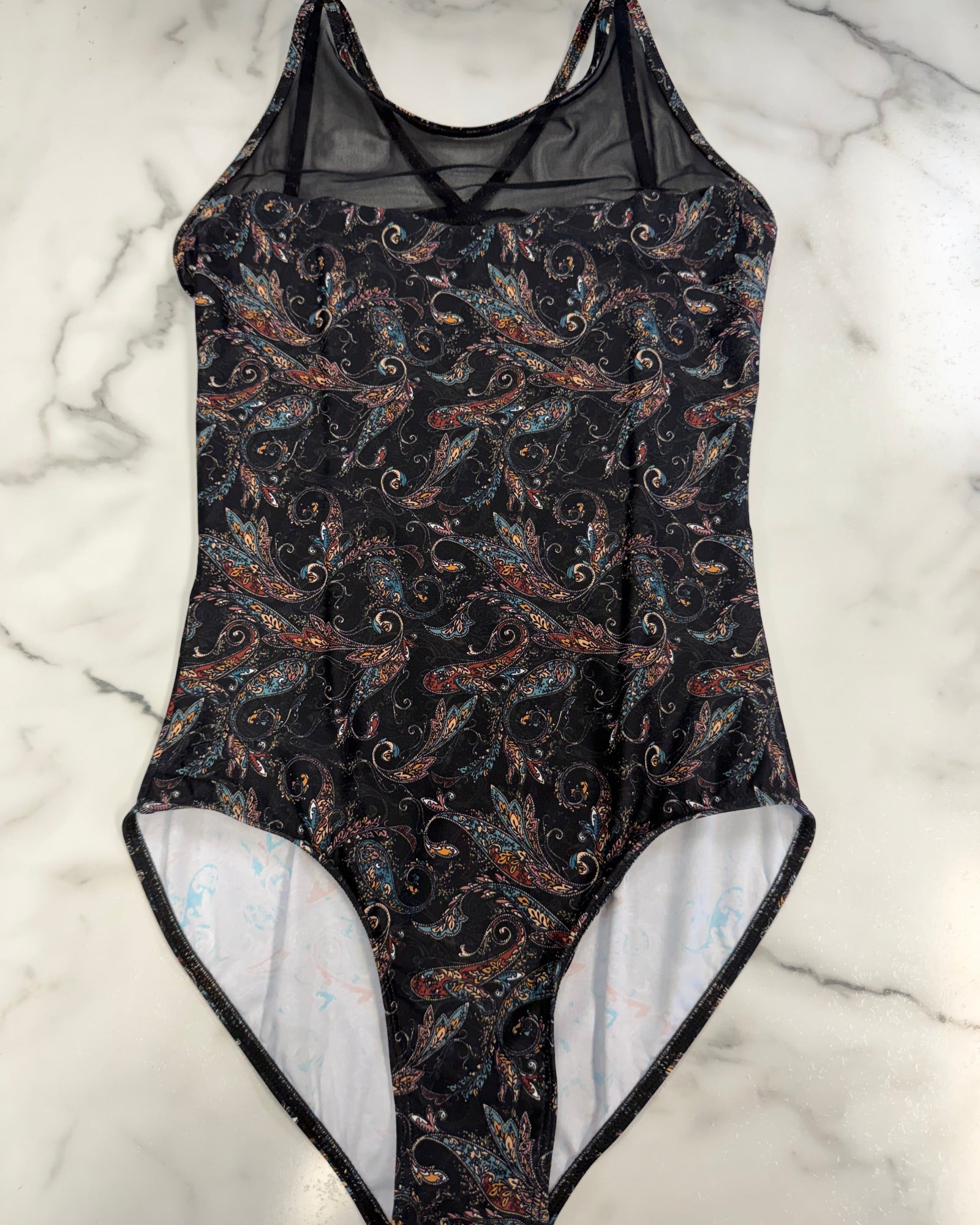 A leotard with a black background and a detailed multicolor paisley pattern, laid flat on a white marble surface.