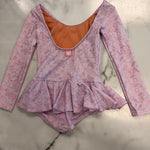 A children's long-sleeve leotard in light purple with a pink floral pattern, featuring a ruffled peplum waist and a contrasting orange inner lining, laid flat on a white marble surface.