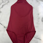 A solid burgundy halter-neck leotard laid flat on a white marble surface.