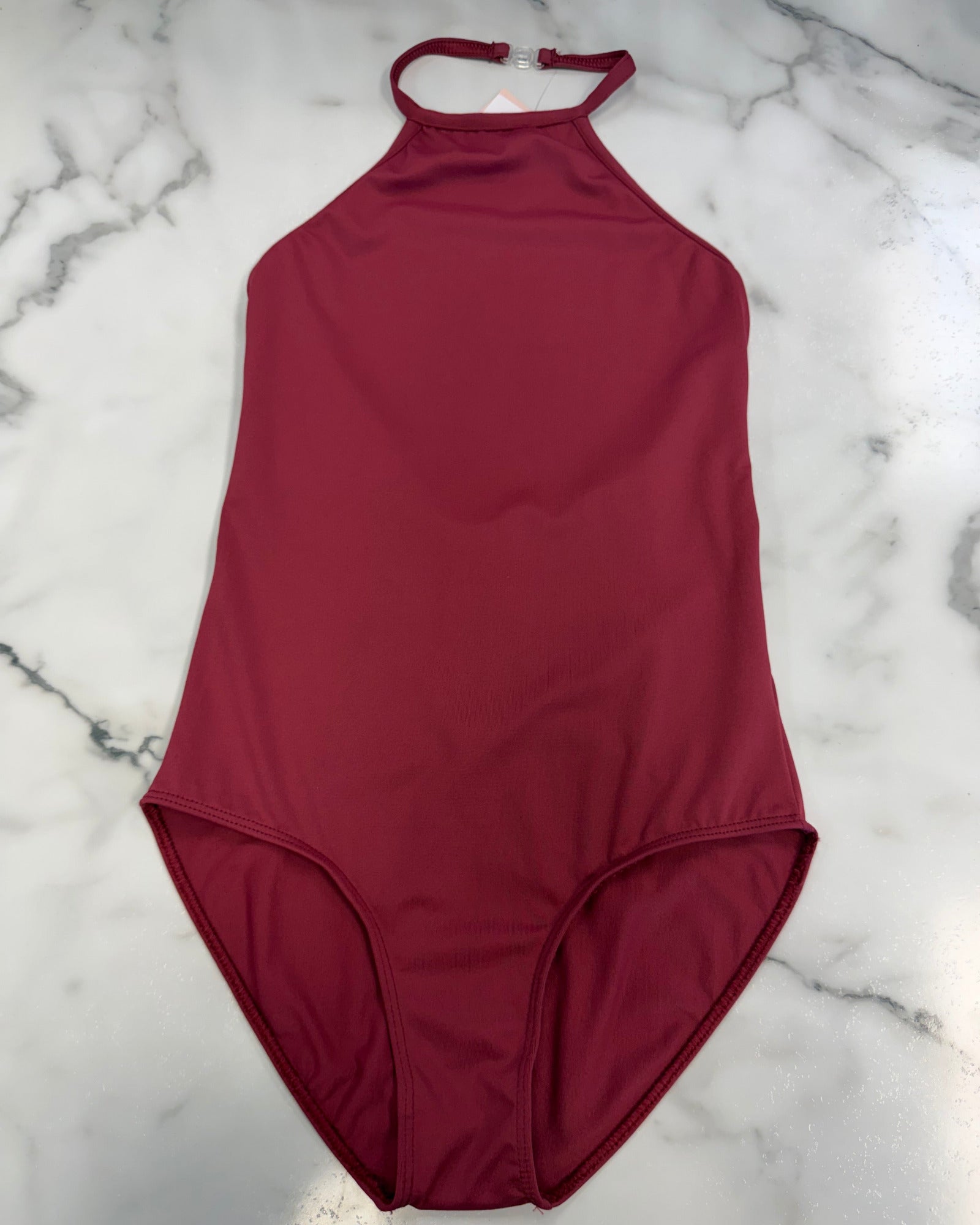 A solid burgundy halter-neck leotard laid flat on a white marble surface.