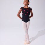 A young girl dancer posing in a black leotard with pink and red floral strawberry patterns, paired with light pink tights and ballet slippers, against a plain white studio background.