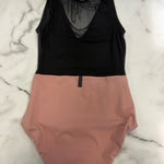A two-tone sleeveless leotard laid flat on a white marble surface, featuring a black mesh upper section and a dusty pink lower section.