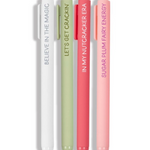 Four slim retractable pens in white, sage green, coral red, and light pink, standing upright on a white background. Each pen has a matching cap and vertical text: 'BELIEVE IN THE MAGIC,' 'LET'S GET CRACKER,' 'IN MY NUTCRACKER ERA,' and 'SUGAR PLUM FAIRY ENERGY.