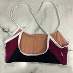 A color-blocked dance bra laid flat on a white marble surface, featuring a nude lining, burgundy side panels, a black bottom panel, and white straps with white trim.