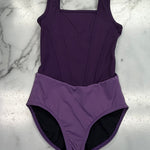 A purple leotard laid flat on a white marble surface, featuring a darker purple bodice and a lighter purple high-waisted bottom with a black lining visible at the legs.