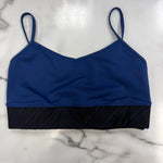 A royal blue dance bra with thin shoulder straps and a black textured horizontal band at the underbust, laid flat on a white marble surface.