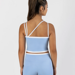 A woman shown from the back wearing a light blue two-piece dancewear set with white trim, consisting of a cropped tank top with crisscross straps and matching high-waisted shorts, against a light gray studio background.